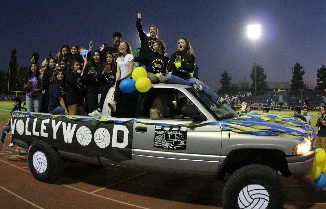 Seniors Erica Mallari and Lissa Favela sit on top of the truck's roof cheering to the crowd as they ride around the track during homecoming.