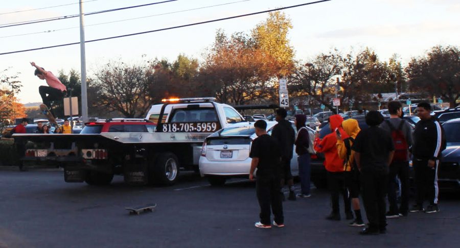 A+teenager+ollies+off+the+back+of+a+tow+truck+parked+in+the+plaza+while+spectators+watch+and+record+the+stunt.+