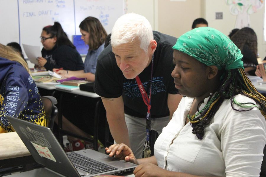 English teacher Ron Baer helps a student with her laptop during period three on April 11.