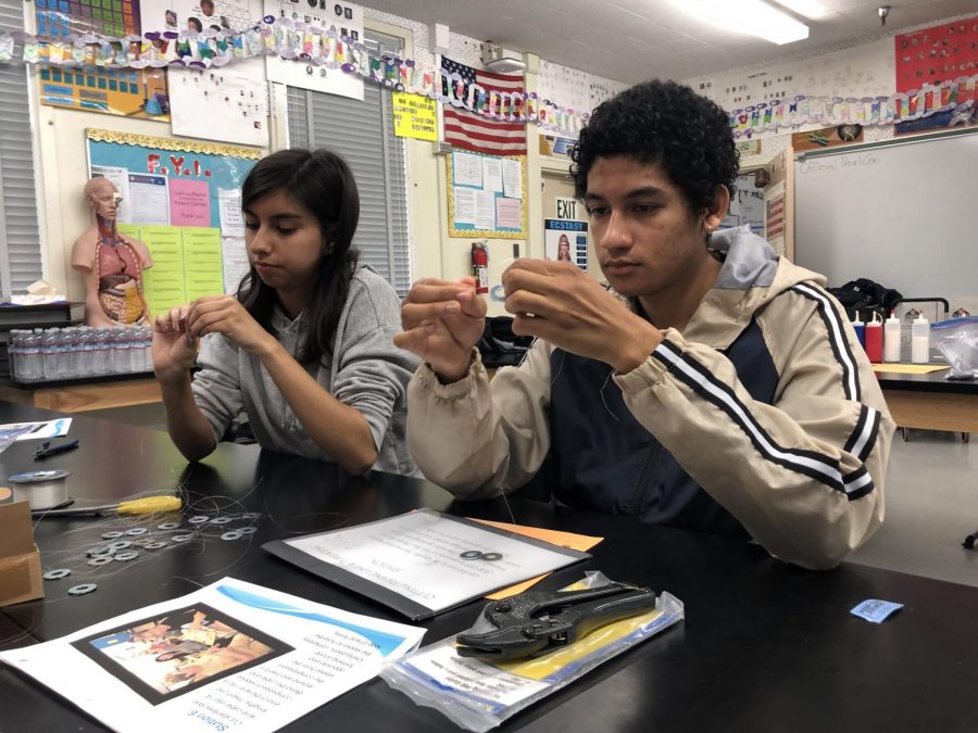 Seniors Emely Felix and Andres Perkins help tie strings to metal washers during WAPI assembly on May 4.