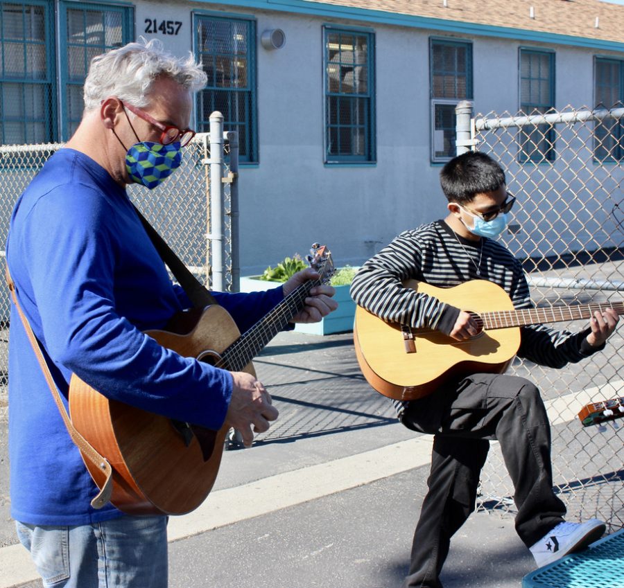 Music teacher Wes Hambright and senior Derek Calderon strum their guitars in the courtyard outside of the music room.