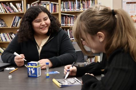 Freshman Nemesi Morales smiles at freshman Serena Elkins while playing Telestrations in the library after school on Tuesday, Jan. 17. Every Tuesday, the library is open after early dismissal for playing games. 