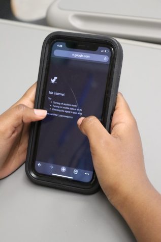 A student holds a phone, which displays a no internet connection screen.