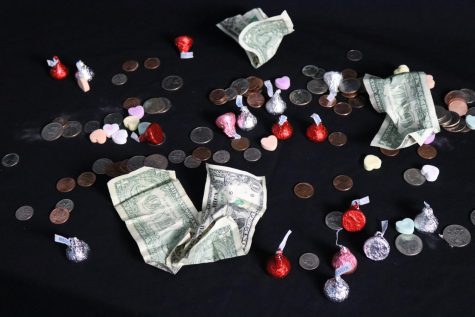 A scattered collection of coins, dollar bills, Hershey Kisses and candy hearts lie on a table, representing Valentine’s Day and the consumerist culture surrounding it. Shopping for the holiday may be fun, but by doing so the buyer actively partakes in the capitalistic nature of the money-making event, rather than declaring their love. 