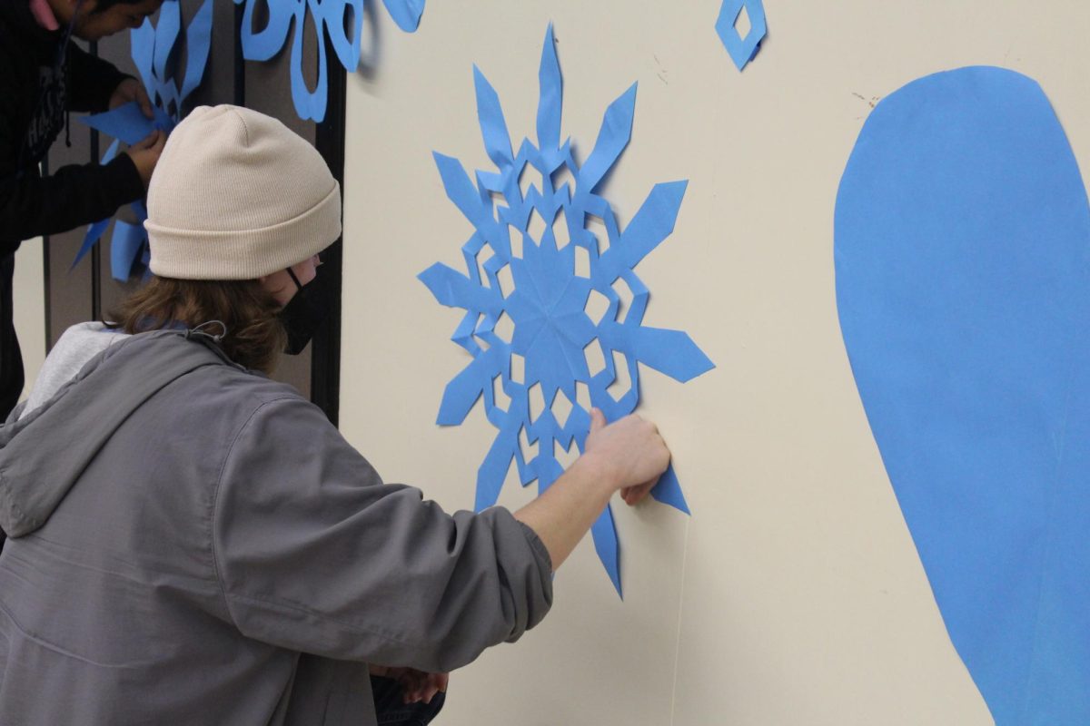Senior Liam Curran tapes a paper snowflake to the MPR wall on Feb. 14 while decorating for the winter dance.